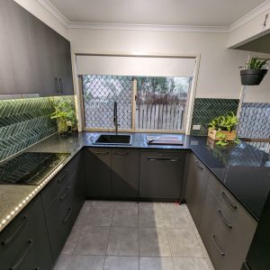 Cool green herringbone mosaic tiles feature in this striking kitchen with black cabinetry by Gecko Kitchens, Brisbane,